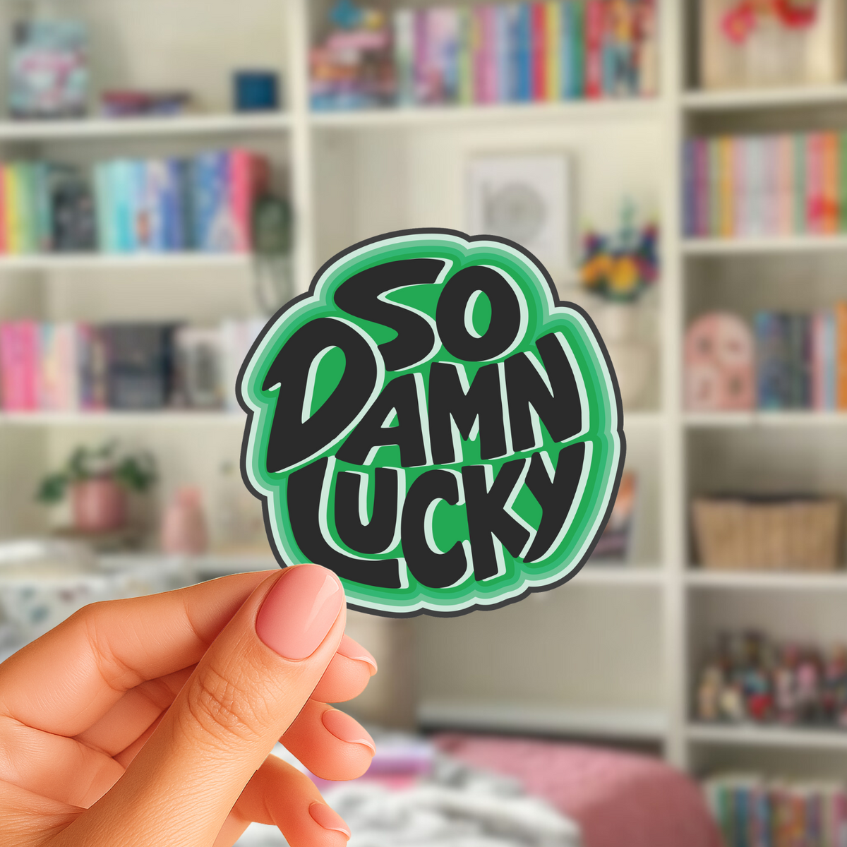 A hand holds a green and black die-cut sticker that reads 'SO DAMN LUCKY' in stylized lettering.